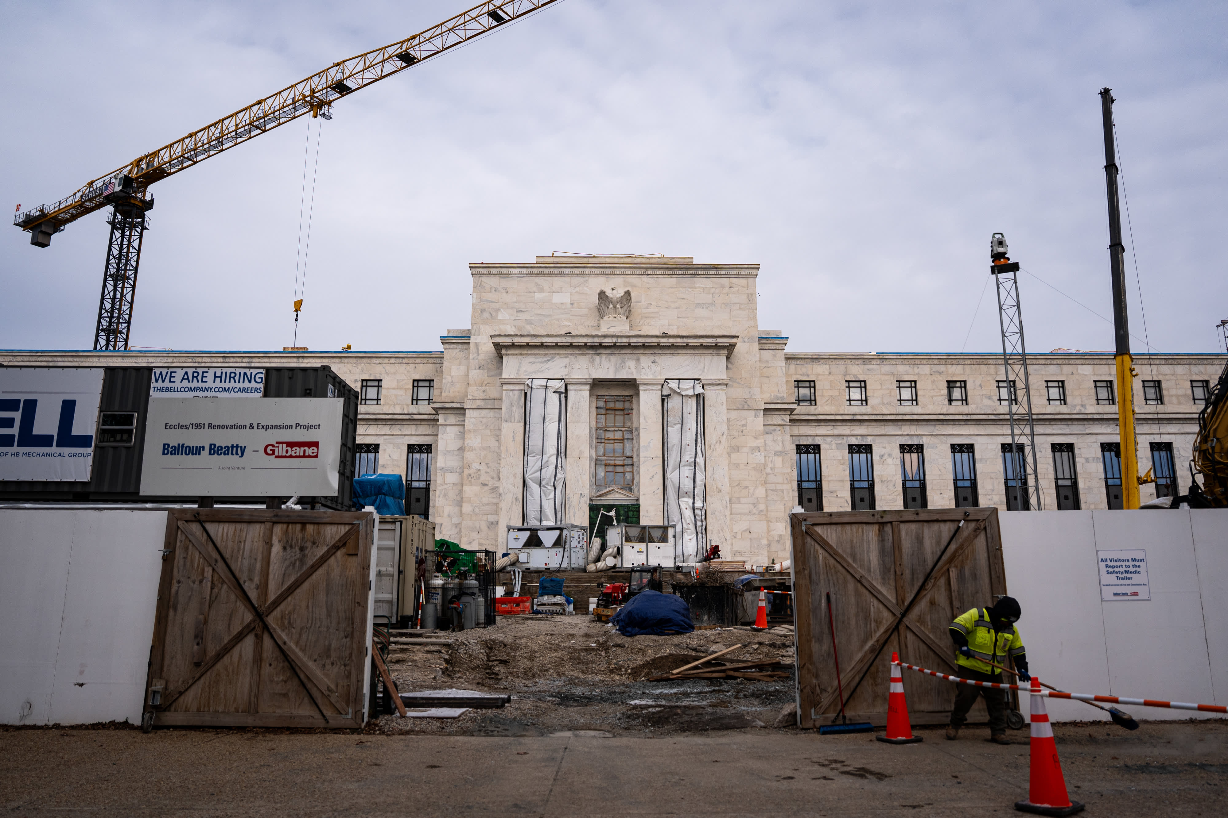 A construction site is shown in front of a government building with a crane, construction workers, and various equipment