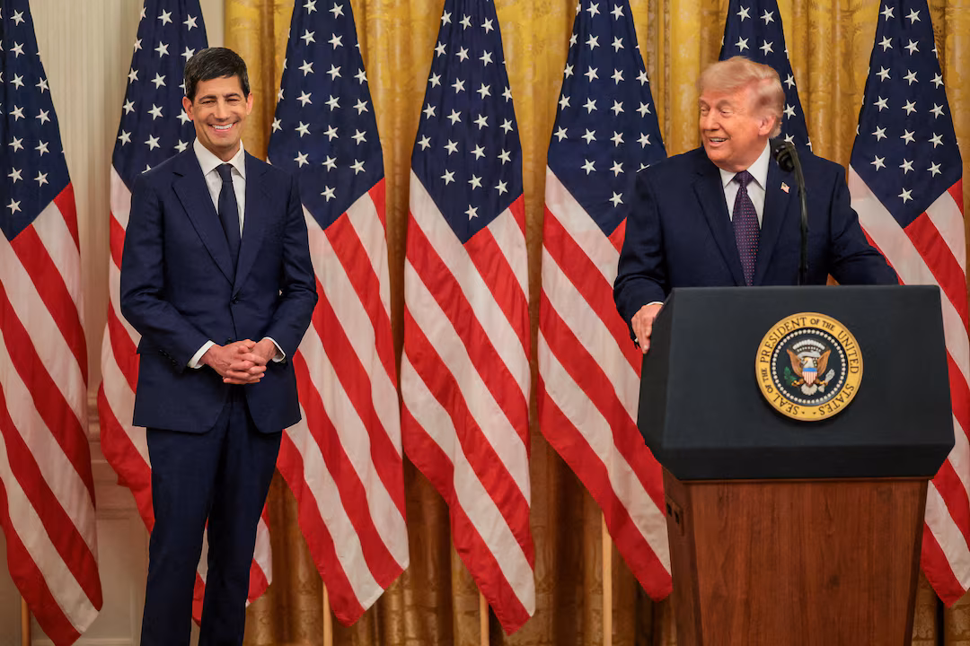 Kevin Warsh 與 Donald Trump 在一場正式活動中合影,背景有多面美國國旗。